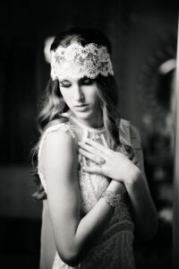 Vintage black-and-white photo of a woman in lace headband and detailed dress, looking down with graceful, elegant poise.