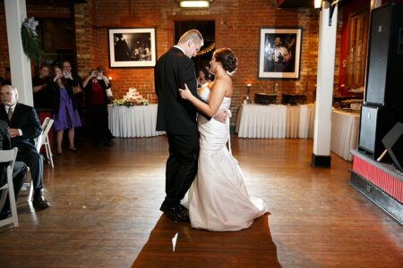 Bride and groom’s first dance in a warmly lit Louisiana reception hall, guests watching and taking photos.