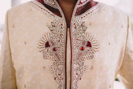 Ornate cream sherwani with gold and red embroidery, beadwork, and patterns; collar also embroidered in red and gold.