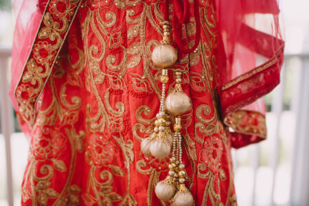 Red and gold embroidered fabric with floral patterns and ornate gold tassels, typical of South Asian attire.
