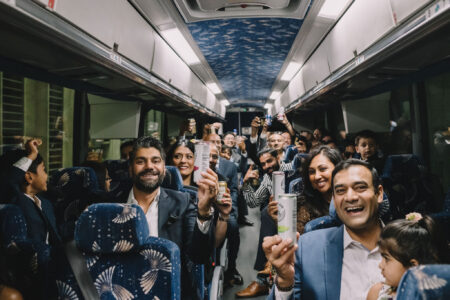 Formally dressed people, including adults and kids, smiling and raising drinks on a lively, celebratory bus.