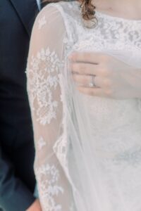 Bride in lace dress displays engagement ring on chest beside partner in dark suit—Louisiana wedding inspiration moment.