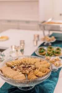 Glass platter with crackers and pecans on teal runner, with appetizers and trays behind for Louisiana wedding inspiration.