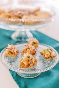 Bite-sized appetizers with creamy topping and garnish on a glass plate, perfect for Gulf South weddings, teal cloth beneath.