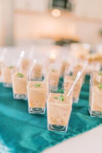 Mini clear cups of creamy appetizer with green herbs and spoons, arranged on teal cloth for a stylish Louisiana wedding.