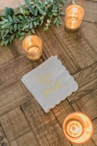 Gold votive candles, a leafy garland, and “love is sweet” napkins on rustic wood—chic New Orleans wedding inspiration.