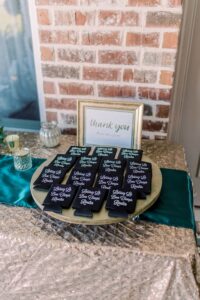 Gold-clothed table with teal runner, navy koozies, and framed Thank You sign at a New Orleans wedding reception.