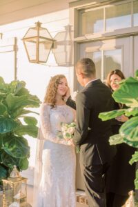 Bride and groom holding hands and smiling at their outdoor Gulf South wedding, with officiant and lush greenery around them.