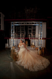 Bride in cream lace gown sits beneath metal arch with candles, lanterns, and dramatic backdrop—Louisiana wedding inspiration.