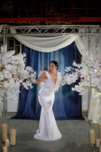 Bride in white gown stands among white floral arrangements, draped fabric, and candles—timeless Gulf South wedding inspiration.