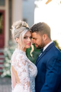 Photo: Sarah Alleman Photography Bride in lace dress looks at camera as groom in navy suit leans forehead to her temple outdoors before New Orleans wedding.