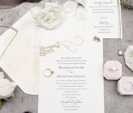 Elegant Louisiana wedding flat lay with invitations, RSVP cards, white roses, rings, jewelry, and pink ring boxes.