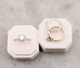 Diamond engagement ring in white velvet box with two gold bands and a diamond ring on light gray surface—wedding inspiration.