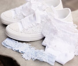 Pearl-accented white sneakers with satin laces beside lace garters, ideal for Gulf South wedding style.
