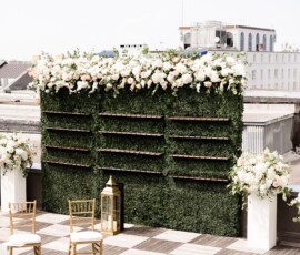 Green hedge wall with flowers and gold chairs on a rooftop, a chic Louisiana wedding reception with city views.