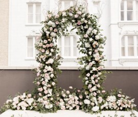 Pink and white floral arch with greenery on a white platform, in front of an ornate white building—ideal New Orleans wedding decor.