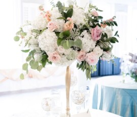 Elegant tall floral centerpiece with white and pink blooms, greenery, candles, and a reserved sign on a lace-covered round table.