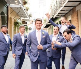 Six men in blue suits playfully pose on a city street, exuding the joyful vibe of a lively Louisiana wedding.