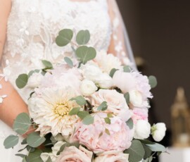Bride in white lace dress with pastel rose and peony bouquet stands at Louisiana wedding; face partially out of frame.