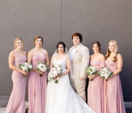 Bride, groom, and four bridesmaids in pink dresses with bouquets pose against a gray wall before a New Orleans wedding reception.