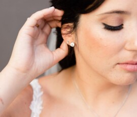 Woman with dark hair in a white dress and diamond jewelry at a wedding, touching her ear with subtle winged eyeliner.