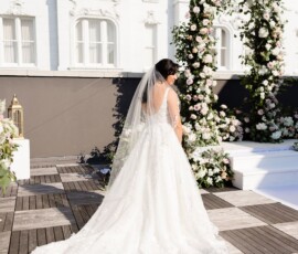 Bride in white gown and veil stands before a floral arch outside a white building—timeless New Orleans wedding inspiration.