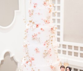 Elegant white wedding cake with pink and gold florals, bride, groom, dog figurines on silver tray; New Orleans vibe.