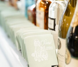 Assorted liquor and wine bottles with light green dog-themed can coolers reading “Cheers! Sansa & Maverick”—New Orleans wedding inspo.
