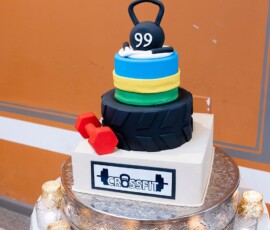 Three-tiered CrossFit cake with kettlebell, weight plates, tire tread, and red dumbbell, surrounded by candles—unique wedding idea.