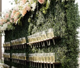 Lush green foliage wall with pastel flowers and shelves of champagne glasses forms an elegant New Orleans wedding backdrop.