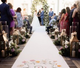 Bride and groom under a flower arch at an outdoor Louisiana wedding, with guests and aisle adorned with candles and lanterns.