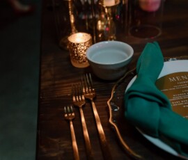 Elegant Louisiana wedding table: dark wood, gold cutlery, white bowl, green napkin, candles, and menu card.