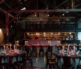 Cozy, rustic restaurant with wood beams, round tables, candles, string lights, and a stocked bar—ideal for intimate Gulf South weddings.