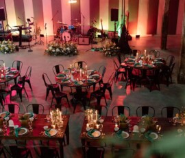 Decorated event space with dining tables, floral centerpieces, candles, and stage under colorful lighting for a New Orleans wedding.