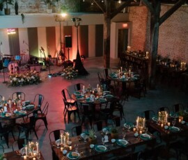 Rustic event venue with wooden beams, set tables, candles, and stage for music—ideal for a New Orleans-style wedding.