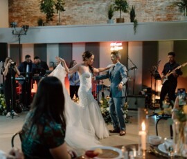 Bride and groom dance joyfully at a flower-filled, candlelit wedding with live band and guests, evoking romantic New Orleans vibes.