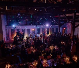 People dance in a dim hall with candles and purple lights, reflecting the lively energy of a New Orleans wedding.