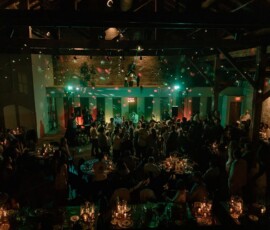 Guests dance under colorful lights at a rustic New Orleans wedding, with candlelit tables and exposed brick walls.