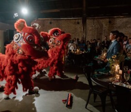 Two red lion dancers perform at an event as guests watch around decorated tables under warm lighting, ideal for New Orleans weddings.