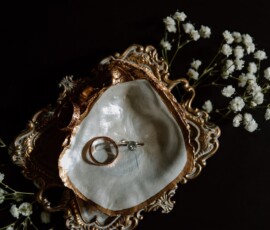 Gold and white dish with rings and earrings on an ornate tray, white flowers, dark background—romantic New Orleans wedding inspo.