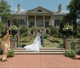Bride and groom kiss on mansion steps at an outdoor New Orleans wedding as guests cheer and take photos.