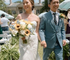Bride and groom walk hand in hand at their Louisiana wedding, surrounded by guests, bubbles, and sunflowers.