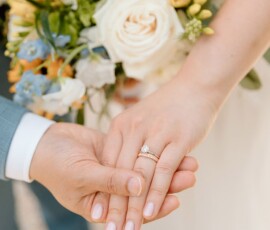 Two hands holding, one wearing a diamond engagement ring, with sunflowers and roses in the background at a New Orleans wedding.
