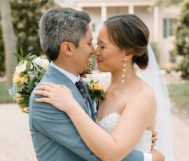 Bride and groom embrace outdoors, smiling lovingly on their Louisiana wedding day; bride with bouquet, groom in light blue suit.