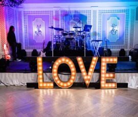 Illuminated LOVE sign in front of a stage with instruments, speakers, and two people at a stylish Gulf South wedding reception.