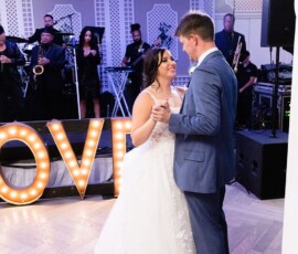 Bride and groom share their first dance at a New Orleans wedding, with a live band and illuminated LOVE sign in the background.