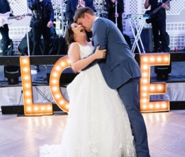 Bride and groom kiss during first dance by lit-up LOVE letters, with live band, at New Orleans wedding.