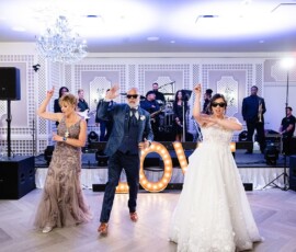 Three adults dance at a New Orleans wedding, live band on stage and illuminated LOVE letters in the background.