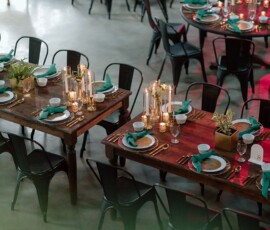 Elegant Louisiana wedding tables with green napkins, gold cutlery, candles, potted plants, and black chairs indoors.