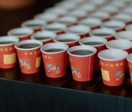 Red paper cups with decorative designs, some filled and some empty, neatly arranged on a black surface for wedding inspiration.